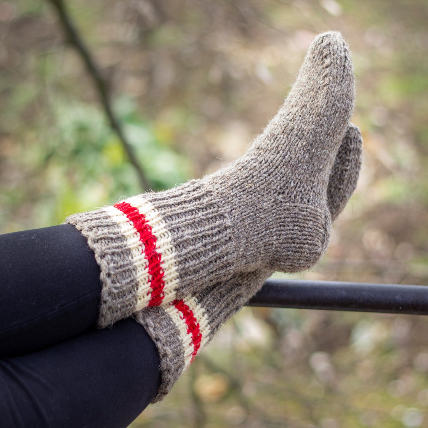Knitted wool socks in beige with three stripes in order: white, red, white, worn on feet and displayed against a natural background.