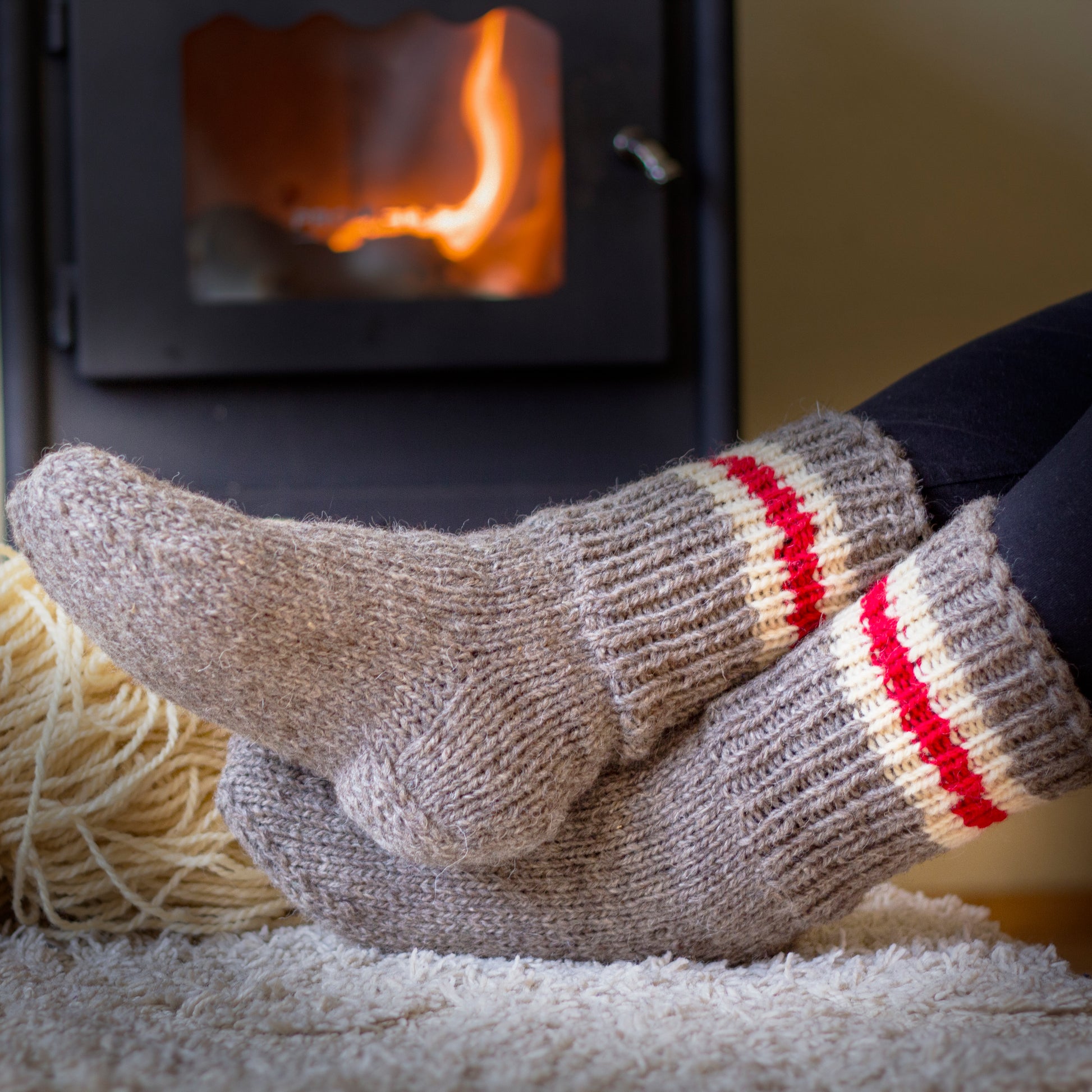Knitted wool socks in beige and 3 stripes in order white, red, white, placed on a burning stove background, creating a warm and cozy atmosphere.