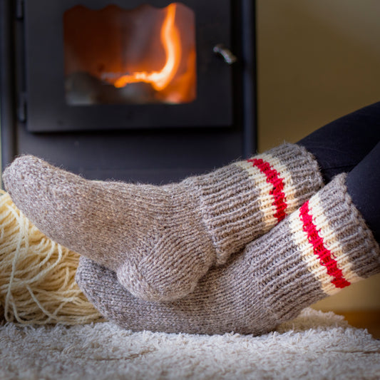Knitted wool socks in beige and 3 stripes in order white, red, white, placed on a burning stove background, creating a warm and cozy atmosphere.