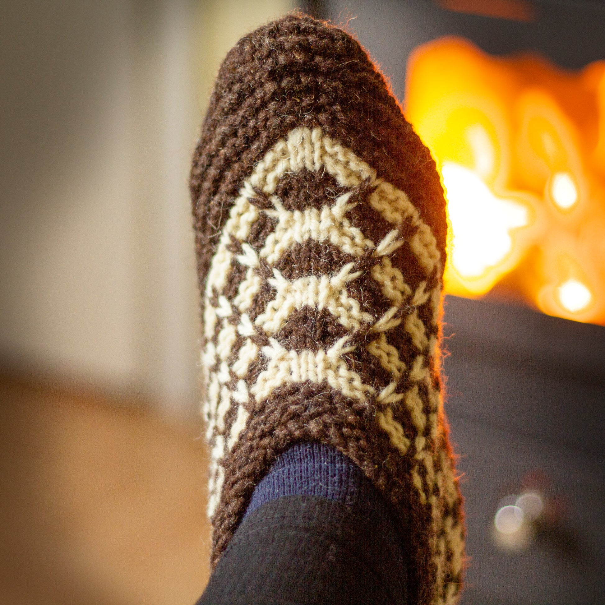 Knitted wool slipper in brown and beige on a burning stove background